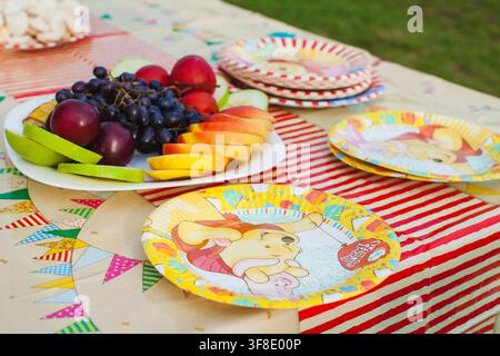 Des fruits frais et des assiettes en carton colorées sont disposés sur une table de fête en plein air. Banque D'Images