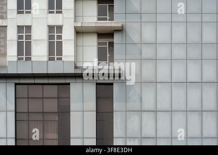 Détail architectural de la façade d'un bâtiment moderne avec des panneaux géométriques gris et des balcons blancs. Banque D'Images