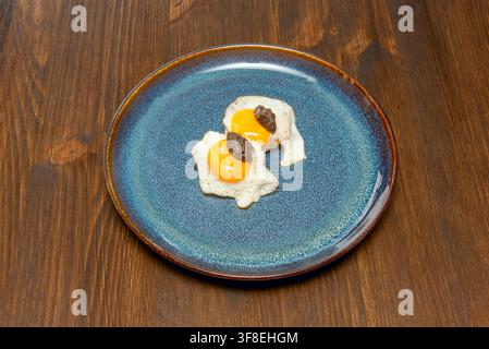 Deux œufs de caille frits garnis de pâte sombre sur une assiette en céramique bleue Banque D'Images