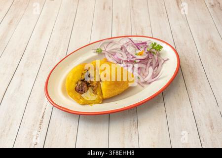Empanada jaune frite coupée pour révéler une garniture de viande et d'œuf, servie avec des oignons rouges tranchés dans une assiette. Banque D'Images