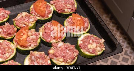 Mettre une plaque de cuisson de rondelles de courgettes farcies dans le four Banque D'Images