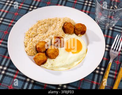 Boulettes de viande avec oeuf côté ensoleillé et flocons d'avoine sur assiette blanche Banque D'Images