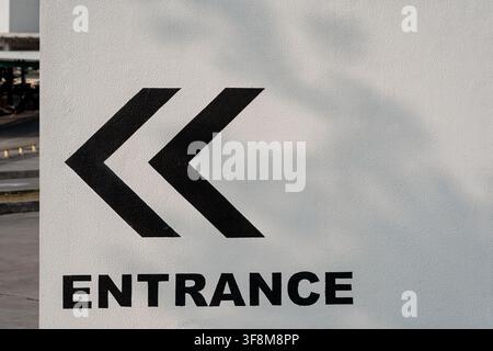 Panneau d'entrée avec flèches directionnelles noires et typographie sur un mur blanc. Banque D'Images