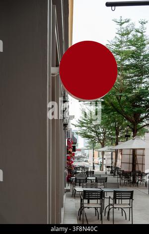 Panneau circulaire rouge vierge sur la façade d'un bâtiment près d'un café de rue en plein air. Banque D'Images