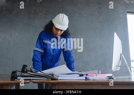 Portrait d'ingénieur portant un casque de sécurité et un uniforme devant un fond gris, paraissant concentré et professionnel, représentant. Banque D'Images