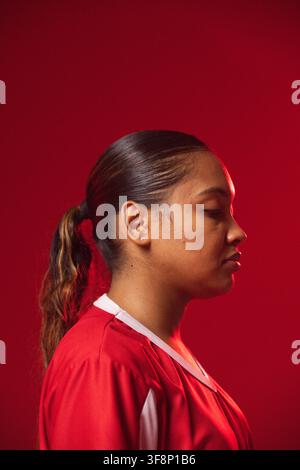 Femme afro-américaine posant dans un studio rouge, portant un maillot de sport, un élastique à cheveux et une boucle d'oreille Banque D'Images
