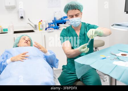 Docteur en blouse de chirurgie et masque préparant une fiole de médicament à côté d'une patiente Banque D'Images