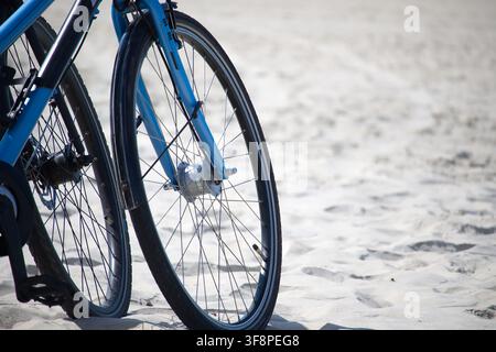 Close-up de roues de vélo bleues posées sur le sable doux de la plage évoquant les loisirs estivaux, le cyclisme en plein air et les voyages côtiers détendus. Composition minimale hi Banque D'Images