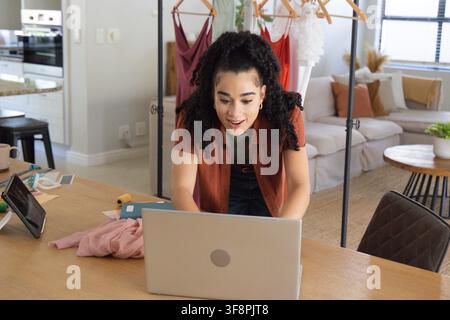 Femme adulte penchée sur un ordinateur portable argenté sur une table de travail en bois à la maison utilisant un mètre ruban jaune Banque D'Images