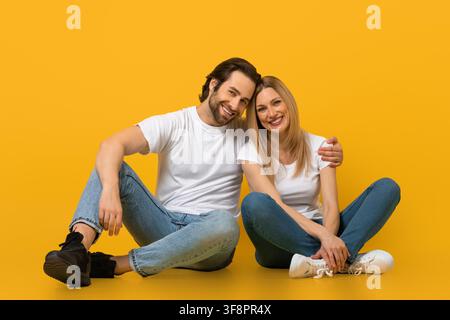Jeun couple heureux souriant et assis ensemble sur fond jaune Banque D'Images