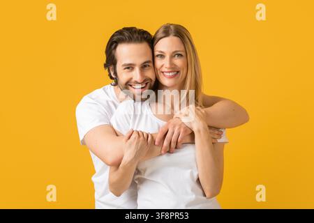 Couple caucasien heureux souriant et s'embrassant devant un fond jaune, concept familial Banque D'Images