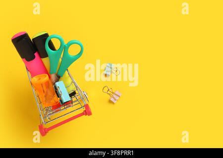 Panier miniature rempli de fournitures scolaires et de bureau colorées sur un fond jaune vif, vue de dessus, les articles sont disposés soigneusement à l'intérieur Banque D'Images