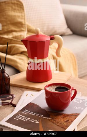 Moka rouge et tasse à café sur une table en bois avec des magazines et une paire de lunettes de lecture, cadre domestique cosy, magazines ouverts avec des articles sur les voyages et r Banque D'Images