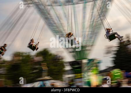 Les passagers du carrousel en mouvement créant une scène de fête foraine dynamique lors d'un festival d'été Banque D'Images