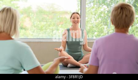 Jeune femme souriante dirigeant un cours de yoga pour des femmes âgées, méditation et pleine conscience pour un vieillissement en bonne santé, style de vie bien-être et fitness Banque D'Images