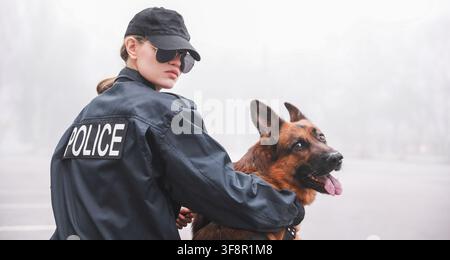 Officier de police féminine en uniforme et lunettes de soleil avec un berger allemand regardant par-dessus son épaule, l'officier regarde par-dessus son épaule, et le chien Banque D'Images