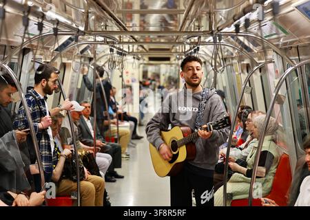 Istanbul, Turkiye - 05 août 2026 : Vue d'un jeune homme jouant une guitare acoustique debout dans un wagon de métro bondé avec des passagers assis Banque D'Images