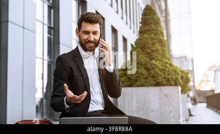 Homme caucasien souriant téléphonant assis à une table de bureau, concept commercial Banque D'Images