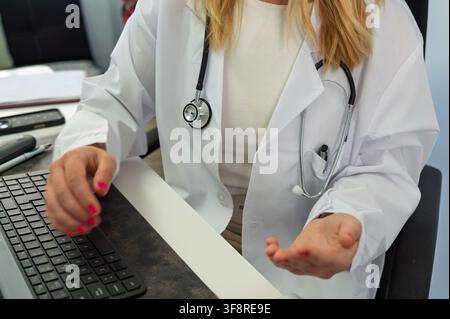 Docteur en blouse blanche et stéthoscope tapant sur un clavier tout en travaillant au bureau Banque D'Images
