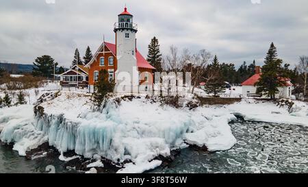 Vue aérienne du phare historique d'Eagle Harbor entouré de rives rocheuses enneigées et des eaux glacées du lac Supérieur à Eagle Harbor, Michigan Banque D'Images