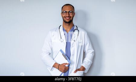 Médecin masculin souriant en blouse tenant un tableau de bord médical, concept de soins de santé Banque D'Images