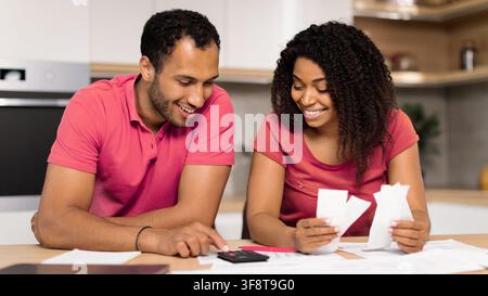 Couple heureux multiethnique faisant son budget ensemble dans la cuisine, utilisant une calculatrice et examinant les reçus Banque D'Images
