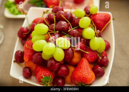 Plateau coloré de fraises fraîches, de cerises sucrées et de raisins verts. Alimentation saine, fruits d'été, dessert et concept de table festive. Banque D'Images