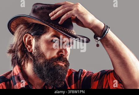 Cow-boy non rasé. Chapeau de cow-boy. Jeune homme séduisant ajustant son chapeau de cow-boy Banque D'Images