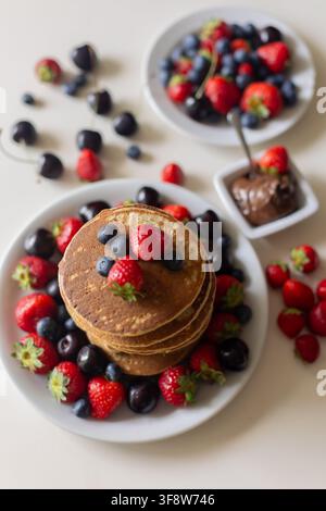 Petit enfant adorable, garçon, mangeant des pancakes américains avec des fraises, des cerises et des myrtilles, arrosés de sirop, chocolat et miel Banque D'Images
