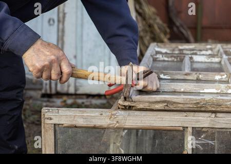 Une vue rapprochée de mains utilisant des outils vintage pour réparer une structure de fenêtre en bois vieillie, représentant un savoir-faire artisanal, des techniques traditionnelles, un Banque D'Images