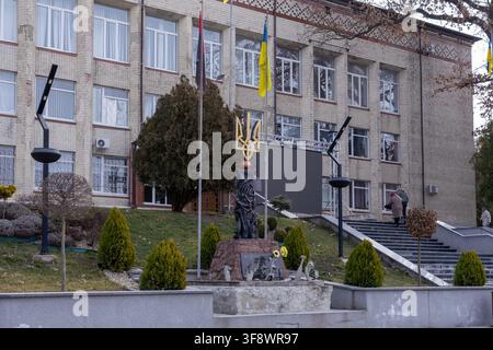 Horodok, Ukraine – 23 mars 2026 : Le monument sculptural représentant un trident doré se dresse devant un bâtiment scolaire, symbolisant l'identité nationale Banque D'Images