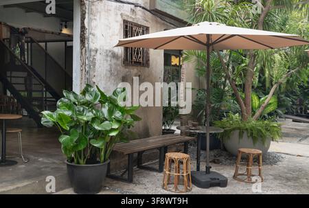 Bangkok, Thaïlande - 10 août 2026 - Un café industriel rustique dans une cour avec des murs en béton usé, un escalier en fer et un siège de jardin serein Banque D'Images