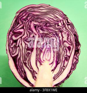 Section transversale d'un chou rouge coupé en deux avec des motifs de feuilles intérieures ressemblant au visage de L'Exclamation, sur un fond vert. Illusion d'optique paréidolie. Banque D'Images
