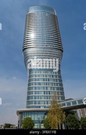 Une vue en contre-plongée d'un gratte-ciel moderne en verre torsadé s'élevant dans un ciel bleu clair à Belgrade, en Serbie. Le soleil se reflète brillamment sur la façade incurvée Banque D'Images