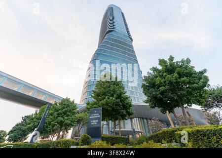 Un plan bas de l’immeuble moderne et sinueux Belgrade Tower à Belgrade, en Serbie, encadré par des arbres verts et un pont piéton. La façade en verre Banque D'Images