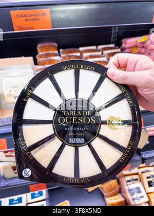Denia, Espagne — 17 juillet 2026. Une personne tient un plateau rond en plastique rempli de différents types de fromage espagnol dans une épicerie. La sélection de fromages Banque D'Images