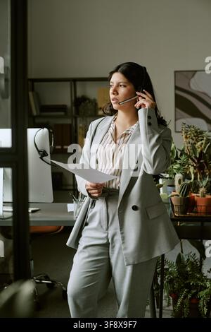 Femme hispanique travaillant dans un centre d'appels tenant un document Banque D'Images