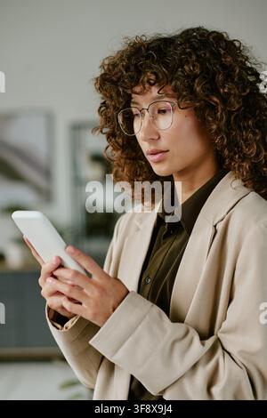 Femme d'affaires biraciale utilisant un smartphone dans un bureau moderne Banque D'Images