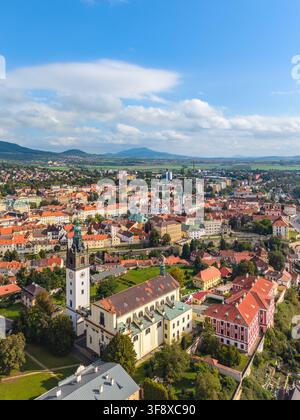 Une vue aérienne magnifique montre la cathédrale Saint-Étienne entourée par la ville vibrante de Litoměřice en Tchéquie. La scène capture une verdure luxuriante et des bâtiments colorés sous un ciel bleu. Banque D'Images