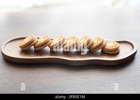 délicieux biscuits sandwich garnis de crème disposés sur une table en bois rustique. Une lumière douce et chaude met en valeur les surfaces texturées des biscuits, la crème sucrée riche Banque D'Images