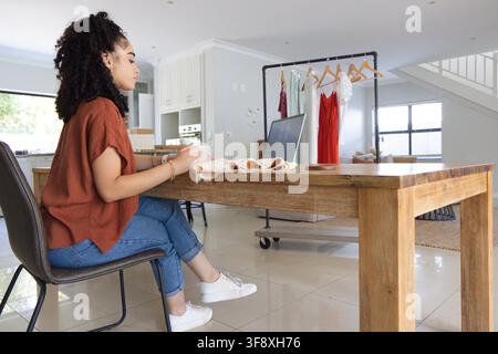 Femme assise à une table en bois dans un studio à domicile, examinant un ordinateur portable et des échantillons de tissus, espace de copie Banque D'Images
