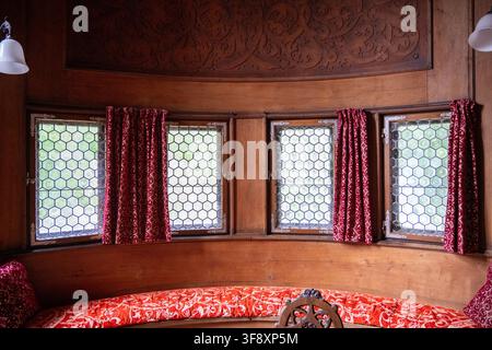 Salle intérieure lambrissée avec des fenêtres à vitraux, des rideaux rouges à motifs et des sièges intégrés à l'intérieur du Mutterturm en Bavière, Allemagne. Banque D'Images