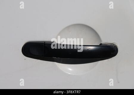 Photo en gros plan d'une poignée de porte extérieure en plastique noir montée sur une porte de véhicule blanche. Banque D'Images