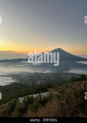 Vue du volcan Mount Agung au lever du soleil sur Bali, Indonésie, avec une mer brumeuse et une ville côtière en contrebas Banque D'Images