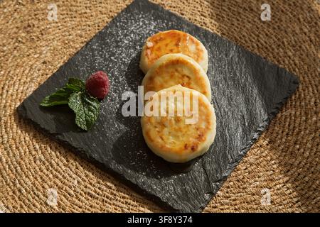 Cheesecakes à la vanille (crêpes au fromage cottage) versées avec du miel sur une assiette noire Banque D'Images