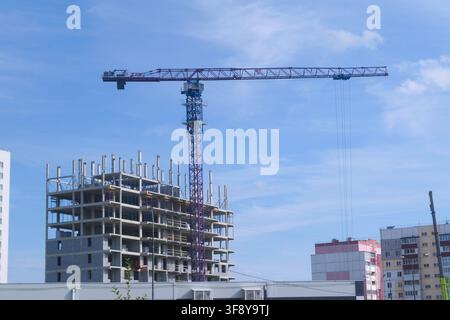 Un chantier de construction présentant une grande grue et un gratte-ciel inachevé, entouré d'autres structures urbaines sous un ciel bleu clair. Le scénario Banque D'Images