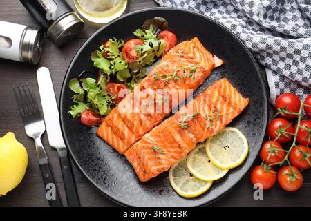 Morceaux de saumon grillé servis avec une salade sur une table en bois, flat lay Banque D'Images