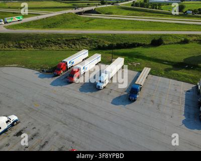 Vue aérienne par drone de semi-remorques et remorques garés à côté d'un chantier de terrassement actif dans le Midwest américain. Banque D'Images