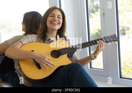 Femme afro-américaine assise près d'une fenêtre tenant une guitare acoustique, montrant une montre et un reflet Banque D'Images