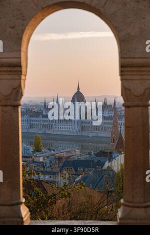Budapest, Hongrie, offre une vue à couper le souffle sur l'emblématique bâtiment du Parlement encadré par une arche historique au coucher du soleil. Banque D'Images
